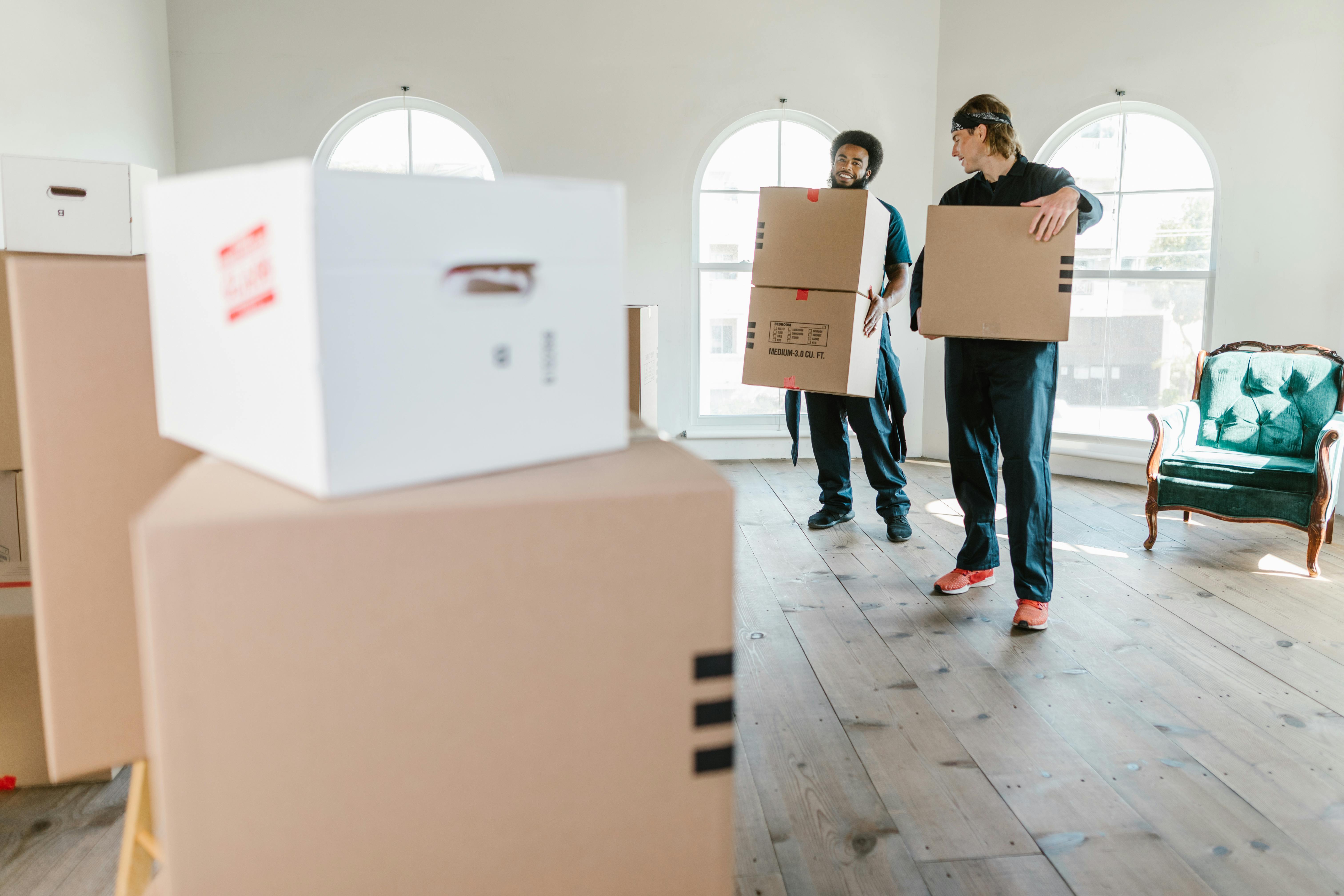Two professional movers carrying boxes through a bright home interior